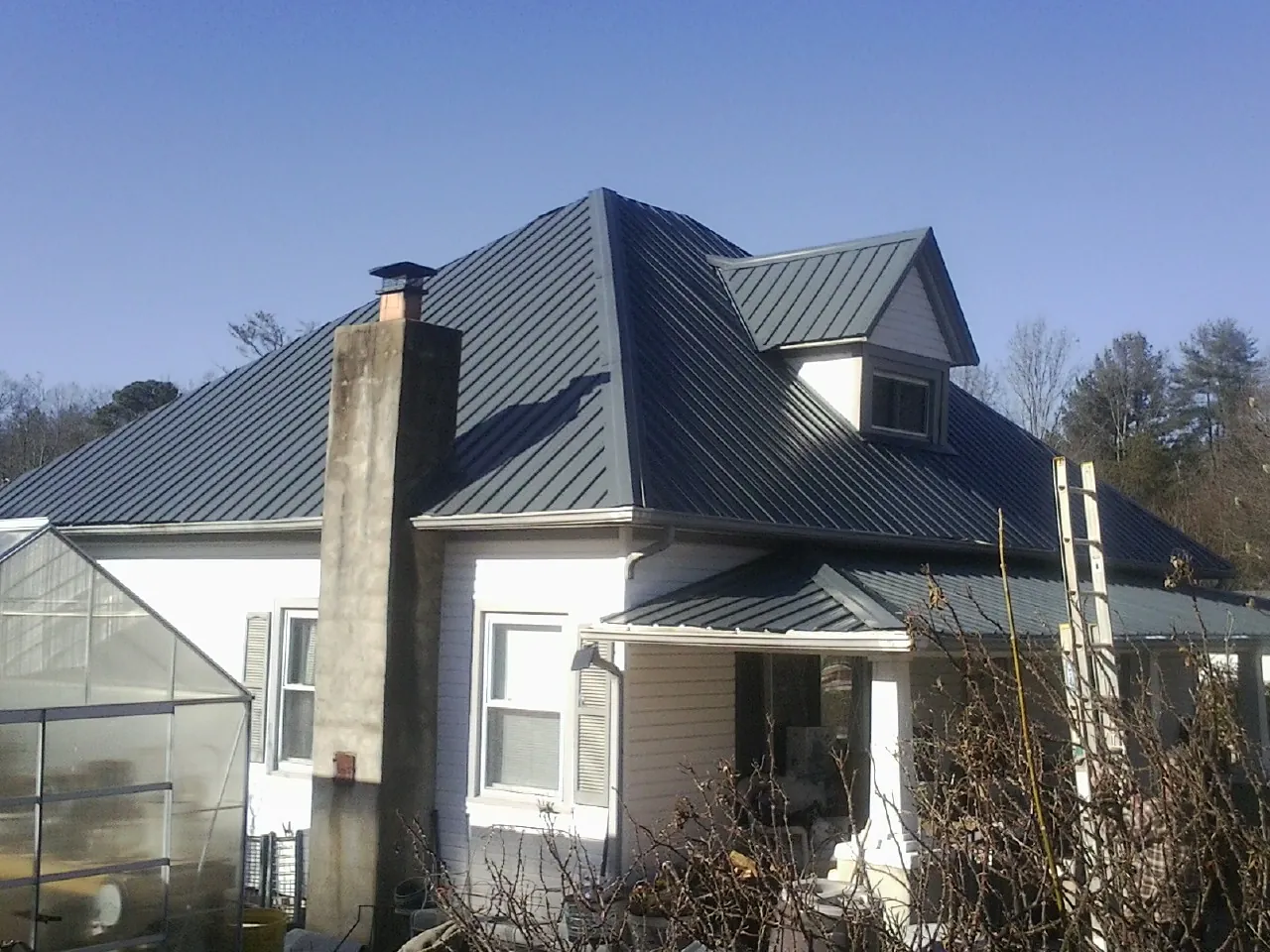 Dark blue standing seam metal roof on a white farmhouse with dormer — Slate & Tile Roof Repair by Roofing Brothers in Smiths Creek