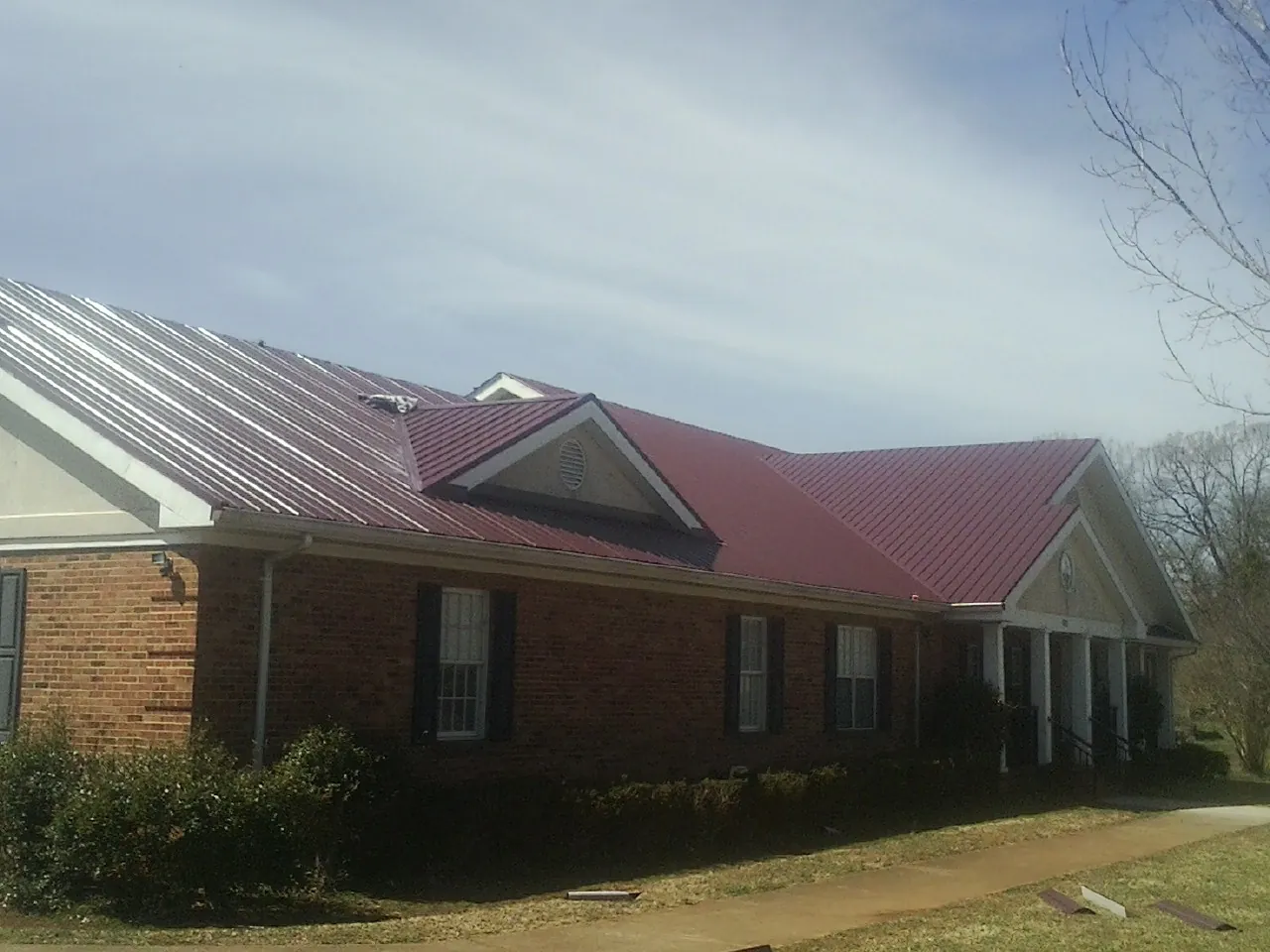Red metal roof with gabled entries on a long brick building, from a Hail Damage Roof Repair job in Smiths Creek