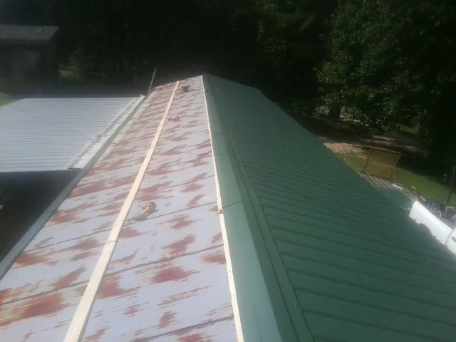 Old rusted panels beside newly installed green metal roofing — Wind Damage Roof Repair by Roofing Brothers in Smiths Creek