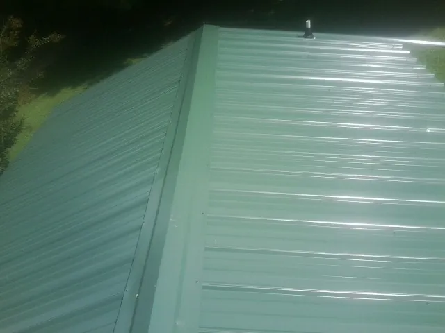 New green metal panels meeting at the ridge of a roof — Flat Roof Repair work by our crew in Smiths Creek