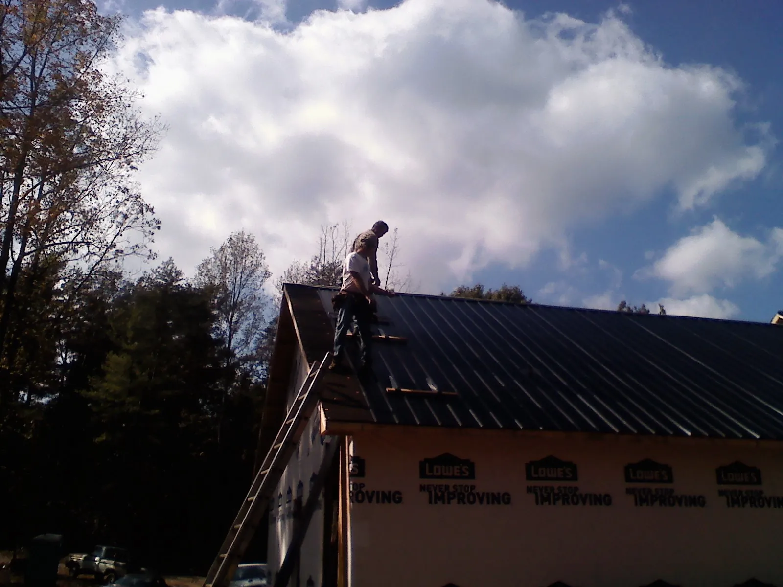 Roofer fastening dark metal panels high against a cloudy sky, from a Roof Inspection job in Smiths Creek