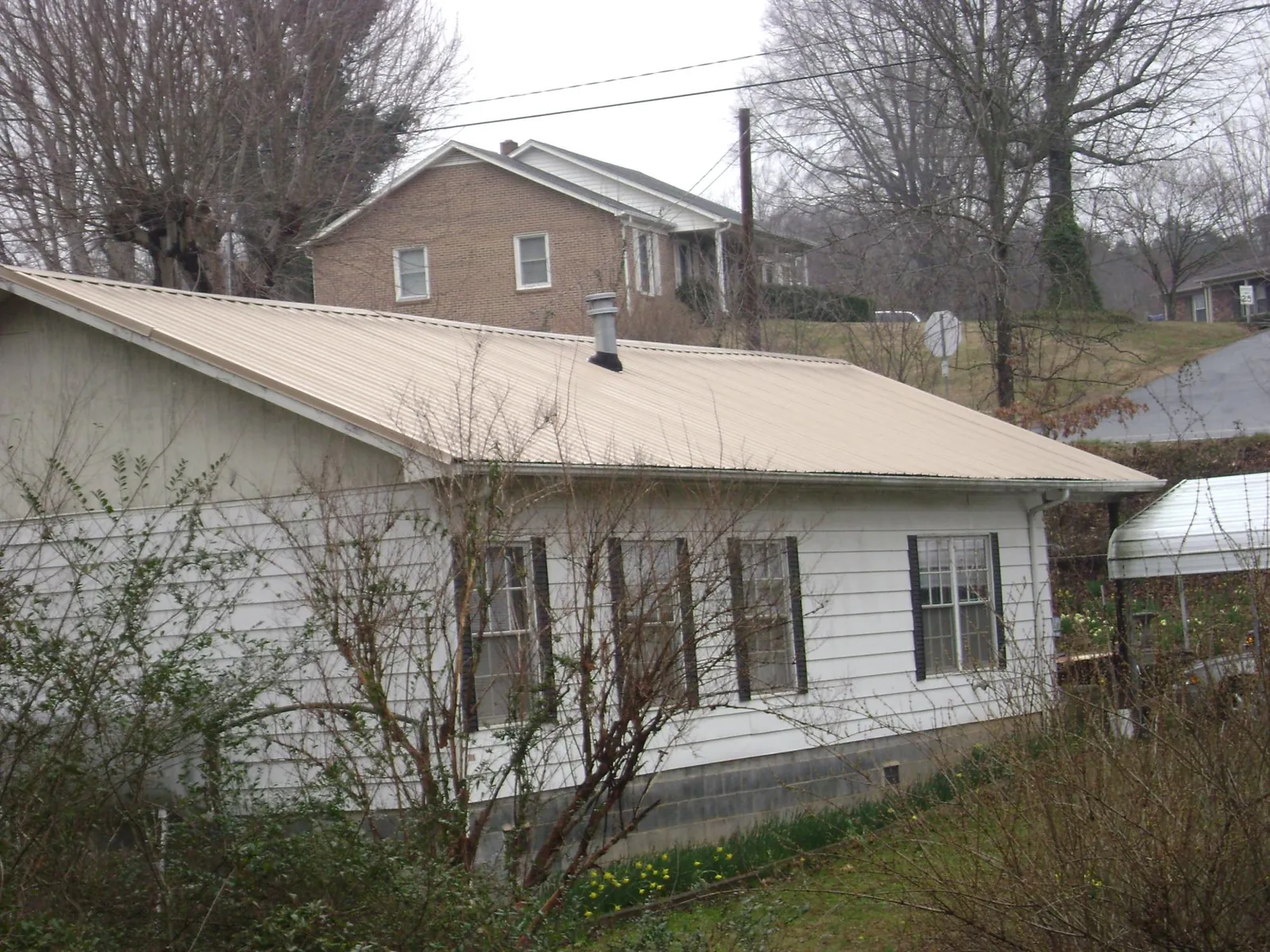 Tan metal roof on a white sided house set into a hillside — Commercial Roofing by Roofing Brothers in Smiths Creek