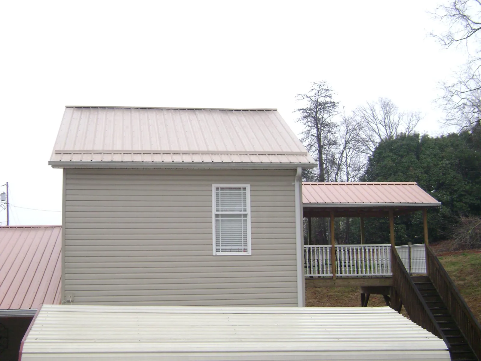 Tan metal roofs on a two story addition and attached porch, from a Roof Replacement job in Smiths Creek