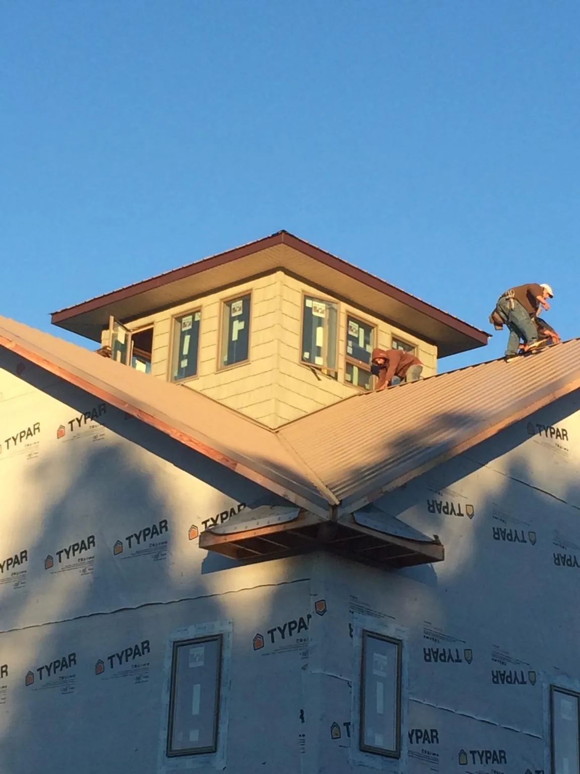Roofers working around a rooftop cupola on a new metal roof at sunset — Roof Waterproofing in Smiths Creek by Roofing Brothers